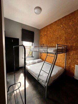 A bunk bed room with a wooden wall, a black door, and a window with blinds. - The Studio (Blackpool)