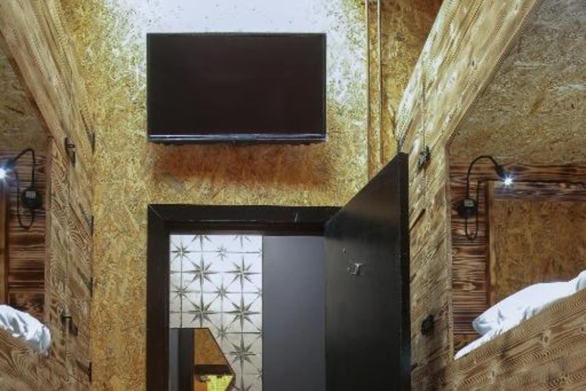 A narrow room with bunk beds, a wooden wall, a small sink, and a mirror.