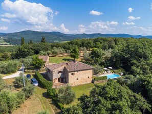 A stone villa with a swimming pool, surrounded by lush greenery and hills.