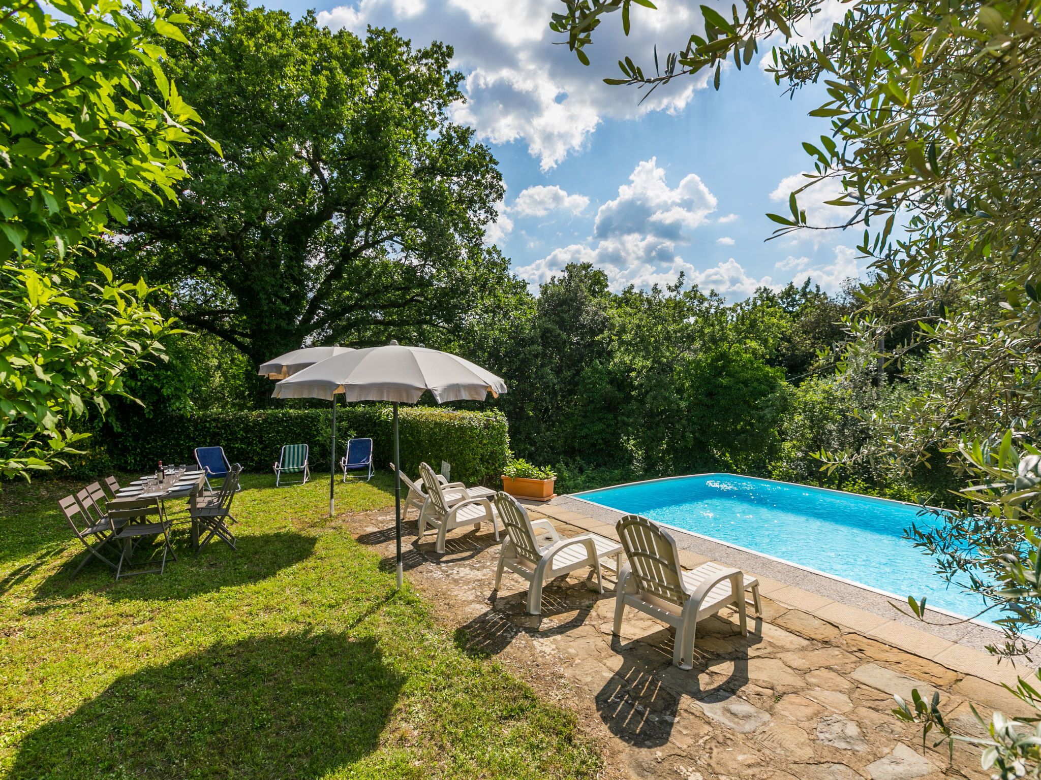 A backyard with a swimming pool, outdoor furniture, and a table set for dining.