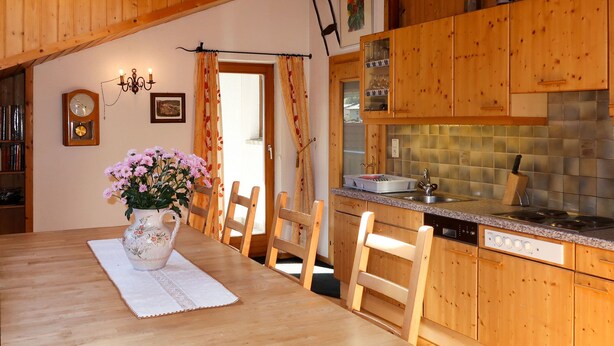 Een houten eettafel met stoelen, een bloemenvaas en een klok aan de muur.