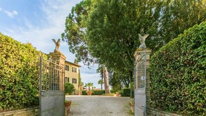 A gated entrance to a property with a gravel driveway leading to a building with a tiled roof. - Giuggiolo 4 by Interhome (Poggibonsi)
