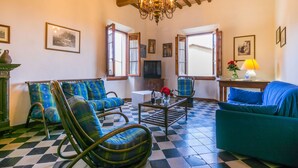 A living room with checkered flooring, two blue armchairs, a sofa, a chandelier, and framed pictures on the walls. - Giuggiolo 4 by Interhome (Poggibonsi)