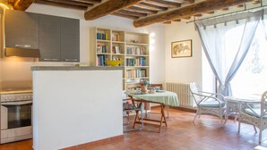 Eine Küche mit Einbauofen, eine Essecke mit Tisch und Stühlen, ein Bücherregal und ein Fenster mit Vorhängen.