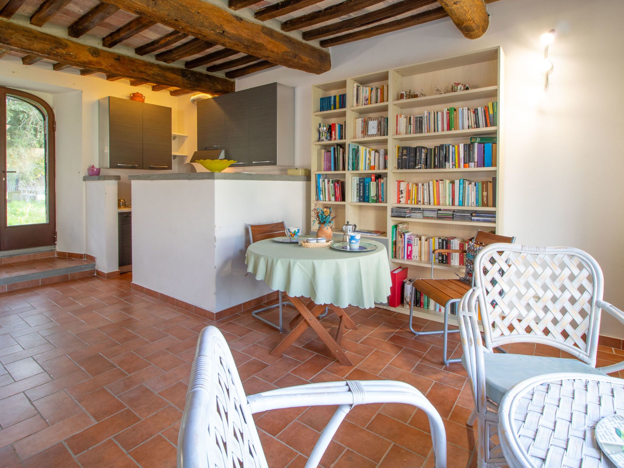A cozy dining area with a round table, white wicker chairs, and a bookshelf filled with books.