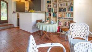 Ein gemütlicher Essbereich mit einem runden Tisch, weißen Korbstühlen und einer Bücherwand voller Bücher.