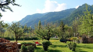 Uma área gramada ao ar livre, com árvores e montanhas ao fundo.