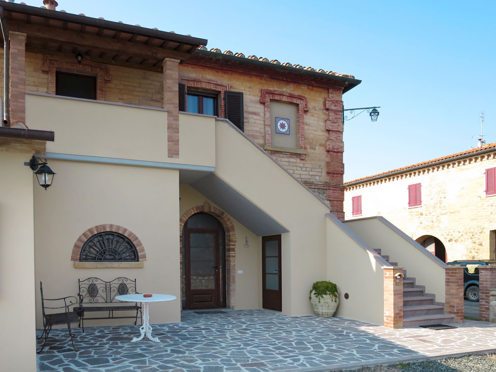 A building with a stone-paved courtyard, a bench, a table, and a staircase leading to an upper level.