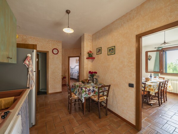 A dining area with a table set for two, a clock on the wall, and a view of the outdoors through a window. - Rustico Cavernoso by Interhome (San Gimignano)