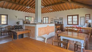 A spacious dining area with wooden tables and chairs, a central bar area with bottles and glasses, and a high wooden ceiling with exposed beams. - Casa alle Vacche by Interhome (San Gimignano)