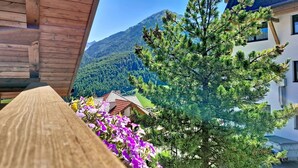 A wooden balcony with a view of a mountain, a pine tree, and a building with a red roof. - Alpenblick by Interhome (Sölden)