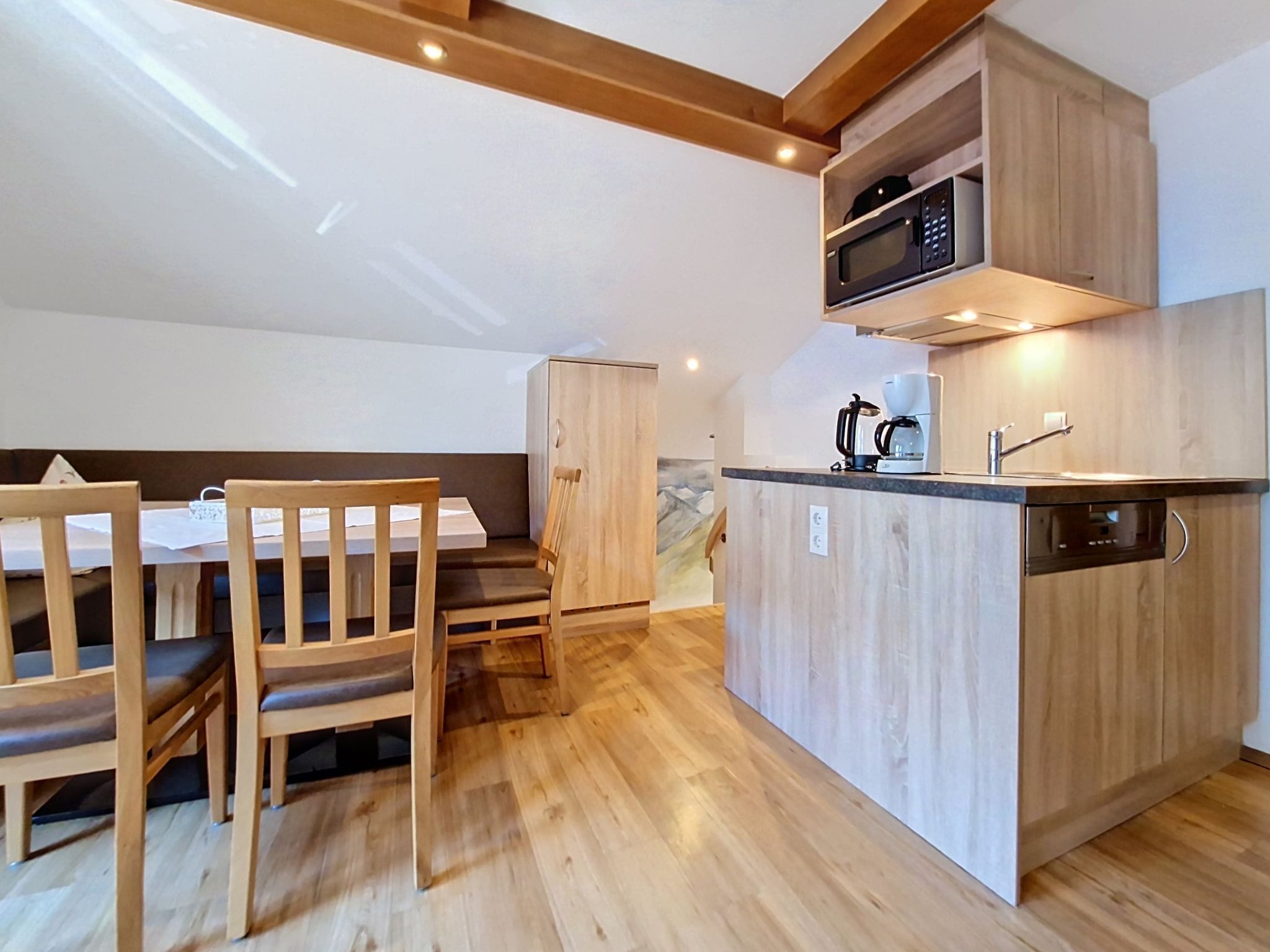 A compact kitchen with a microwave, coffee maker, and a small sink. There is a wooden dining table with chairs and a cabinet.
