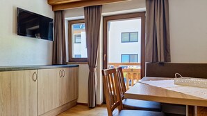 A kitchen with wooden cabinets, a dining table with chairs, and a window with curtains. - Alpenblick by Interhome (Sölden)