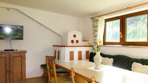 A dining area with a wooden table, chairs, a vase with flowers, a television on a cabinet, and a window with curtains. - Anemone by Interhome (Sölden)