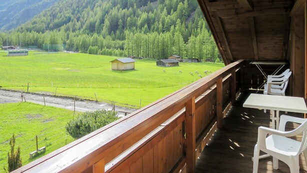 A wooden balcony with a view of a green field, a small building, and a forested mountain in the background. - Anemone by Interhome (Sölden)