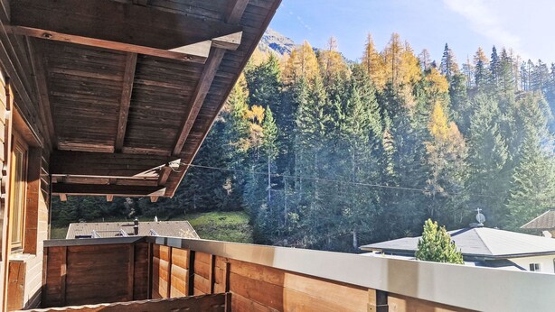 Eine Holzhütte mit Balkon mit Blick auf eine bewaldete Berglandschaft.