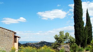 Un bâtiment en pierre à l’aspect rustique, un ciel d’un bleu éclatant et, au loin, une vue sur une colline couronnée de ruines.