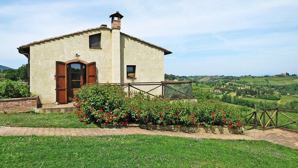 Un pequeño edificio rústico con puerta y ventanas de madera, rodeado de abundante vegetación y vistas panorámicas del campo.