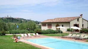 Una piscina con sillones de descanso, un edificio con techo de tejas y vista a un paisaje urbano distante.