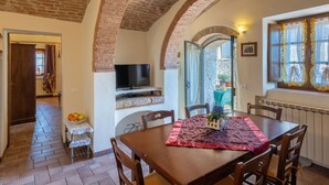Un comedor con techo de ladrillo, un televisor montado en la pared y una mesa con mantel individual y sillas.