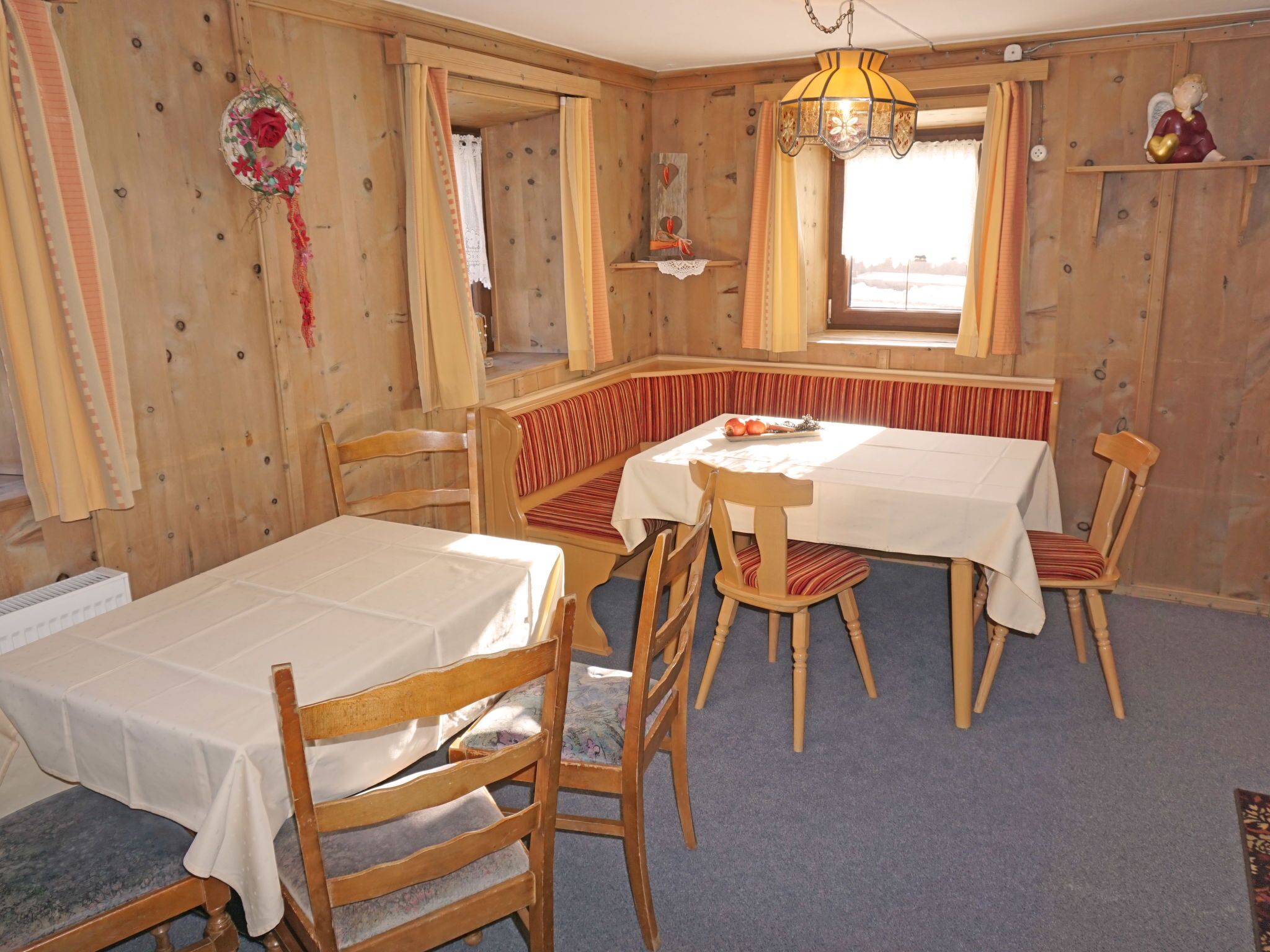 A cozy room with a wooden interior, a dining table with chairs, a bench, and a window with curtains.
