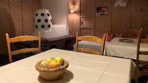 Ruokailutila, jossa on puuseinät, valkoisella pöytäliinalla katettu pöytä ja pöydällä oleva hedelmäkulho.