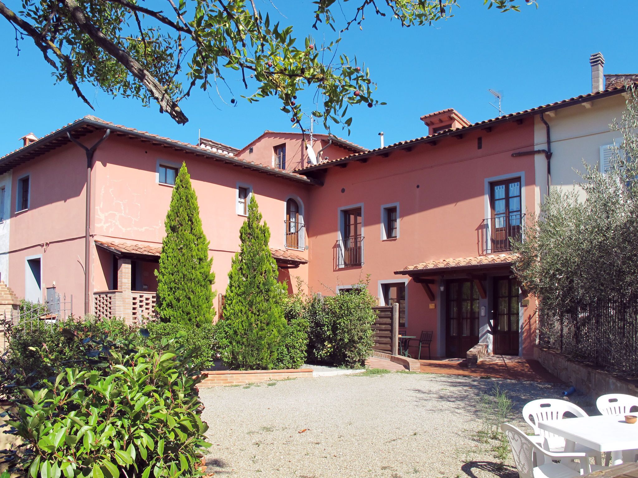 A two-story building with a red facade, a gravel courtyard, and a table with chairs outside.