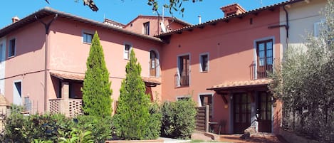 A two-story building with a red facade, a gravel courtyard, and a table with chairs outside.