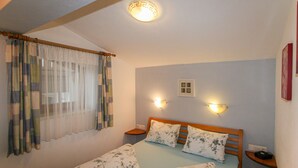 A bedroom with a bed, floral-patterned pillows, a wooden headboard, two bedside tables, and a window with sheer curtains.