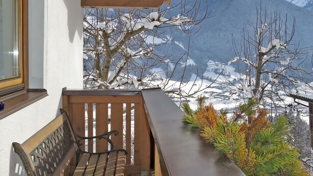 A balcony with a wooden bench and a table, overlooking a snowy mountain landscape.