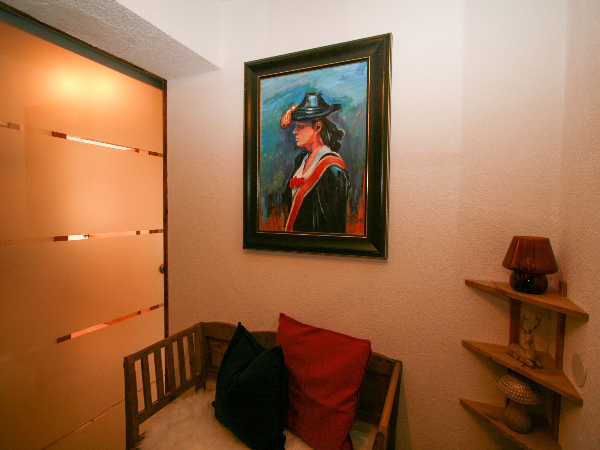 Une pièce avec un berceau, un tableau encadré et une lampe posée sur une étagère.