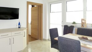 Una cucina moderna con una TV a schermo piatto, una zona pranzo con tavolo e sedie, e una porta in legno che dà su un'altra stanza.