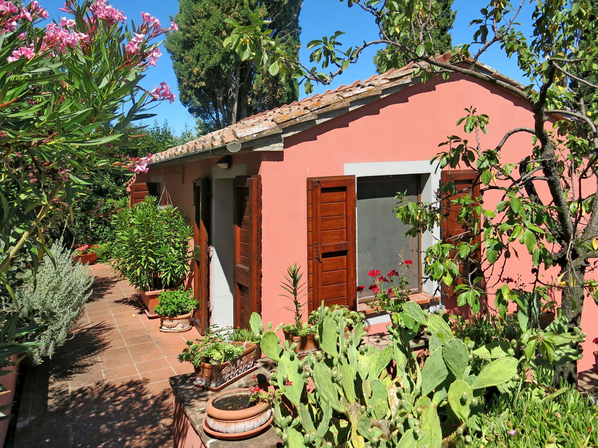 Una casita rosa con techo de tejas, puerta de madera y ventana con contraventanas.
