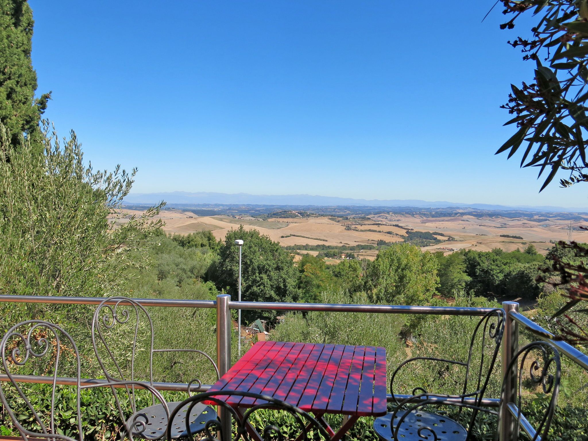 Une table en métal recouverte d’une nappe rouge, entourée de verdure et offrant une vue sur un paysage pittoresque.