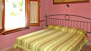 A bedroom with a bed, a window with curtains, a painting on the wall, and a wooden ceiling. - Castagni I (OCT100) by Interhome (Orciatico)