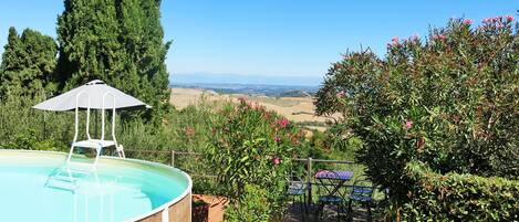 A swimming pool with a pergola and umbrella, surrounded by lush greenery and a scenic view.