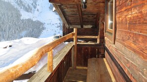 Eine Holzhütte mit einer Holzterrasse und Blick auf eine verschneite Berglandschaft.