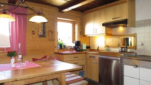 Eine rustikale Küchenzeile mit Holztisch, Bänken, einem Geschirrspüler und einem Fenster.