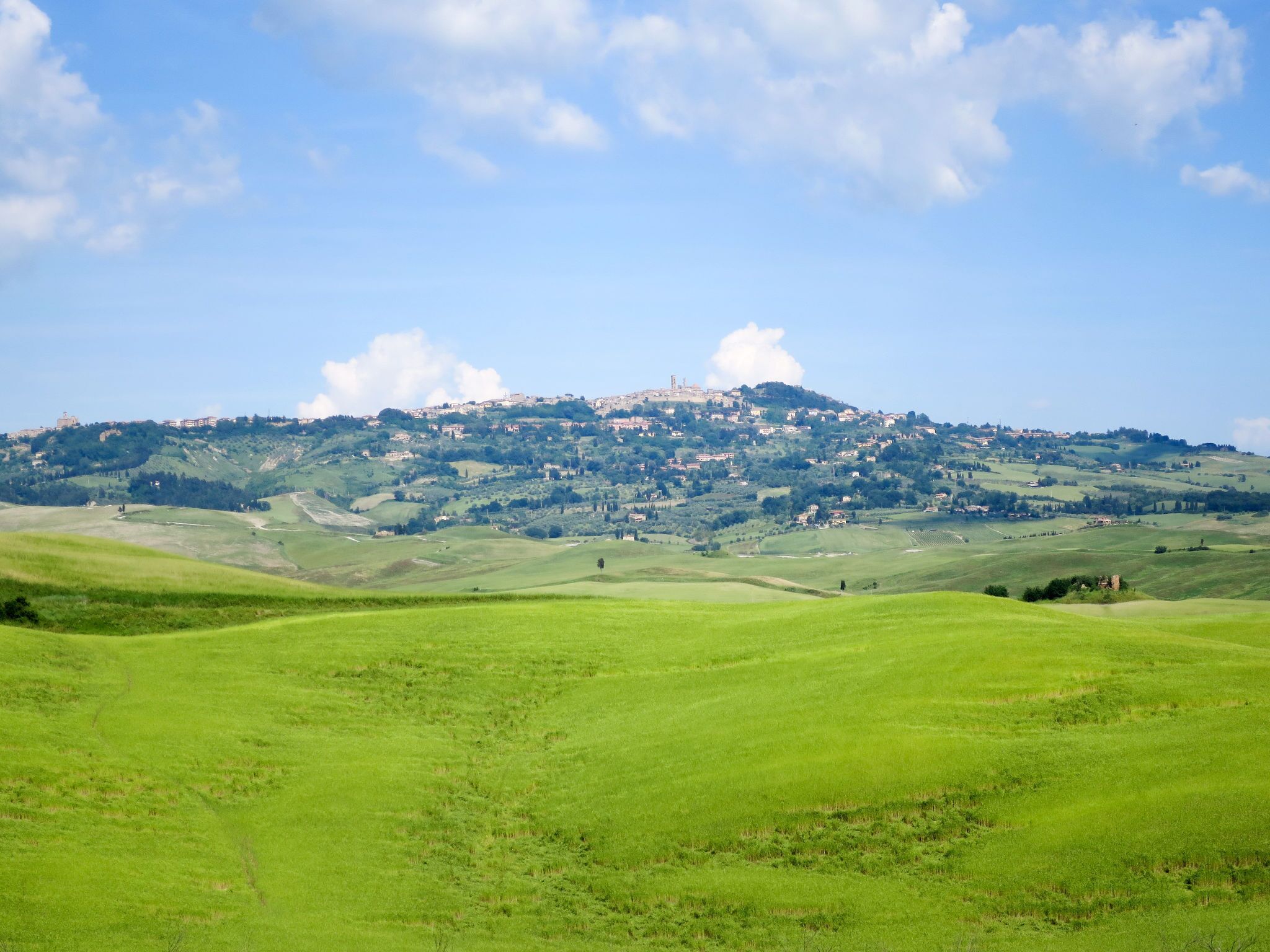 A panoramic view of a green landscape with rolling hills and a distant hilltop settlement.