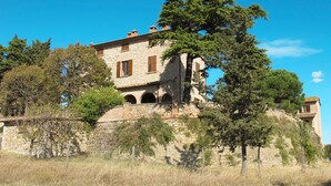 Un bâtiment en pierre doté de fenêtres en arc de cercle et d’un balcon, entouré d’arbres.
