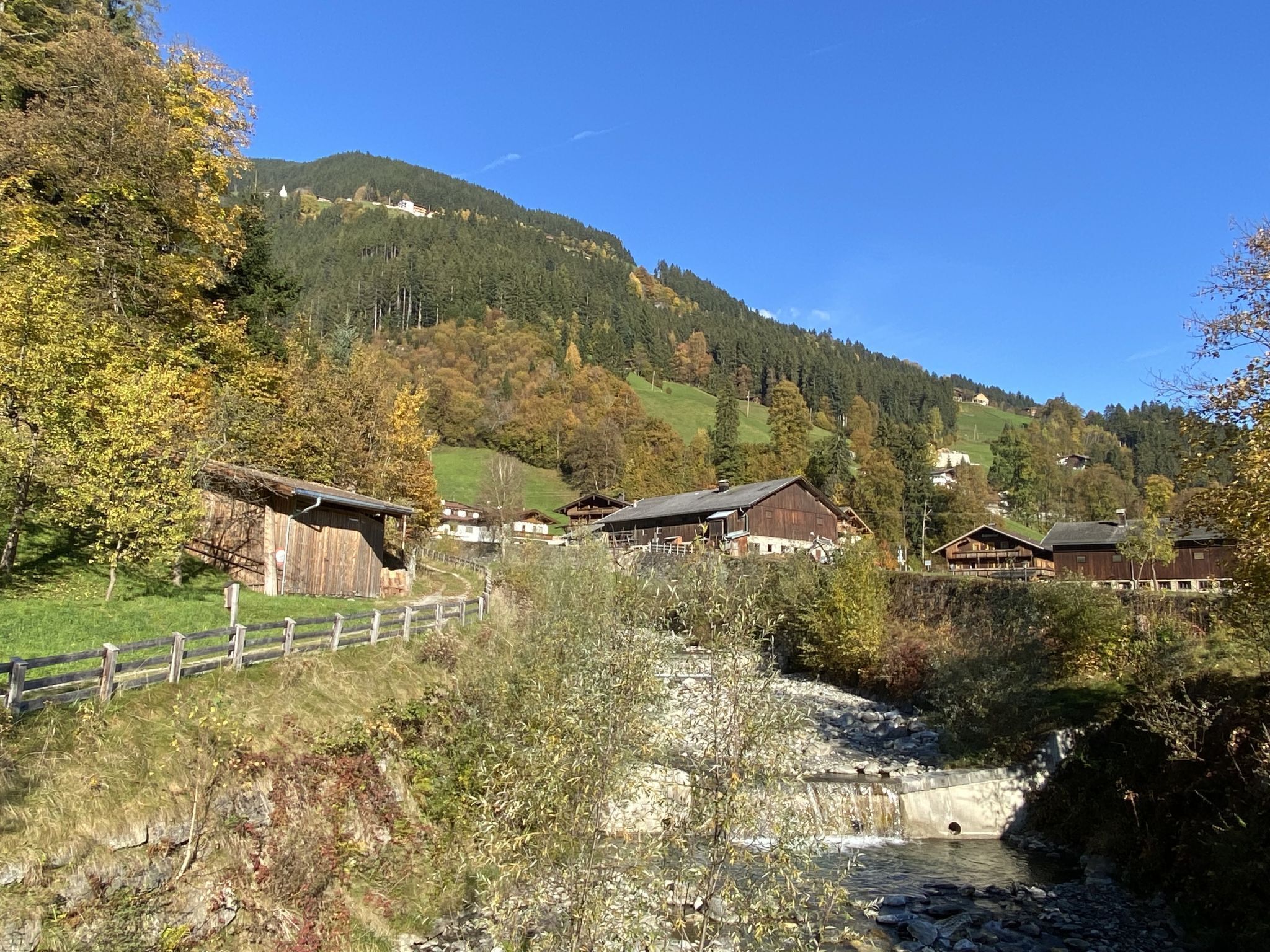 A rural village with traditional wooden houses, a small stream, and a mountain in the background.