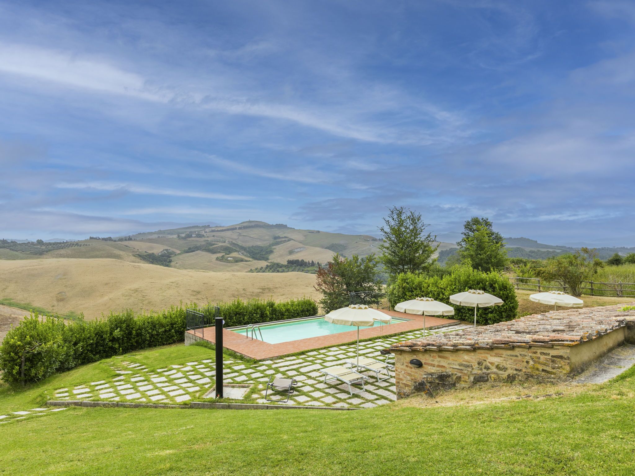 Un espace piscine agrémenté de carreaux de pierre, de chaises longues et de parasols, entouré d’un paysage verdoyant et luxuriant, avec des collines en arrière-plan.
