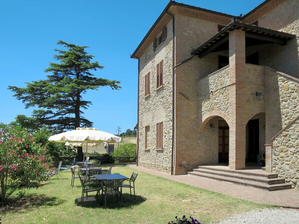 A stone building with a courtyard, outdoor seating, and a large tree.