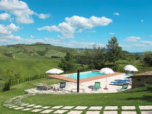 A pool area with a view of rolling hills, outdoor seating, and umbrellas.