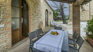 An outdoor patio with a table set for two, surrounded by stone walls and a wooden pergola.