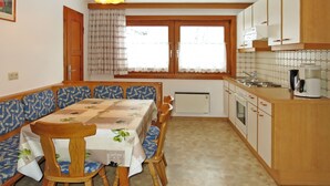 Une cuisine compacte comprenant un coin repas, des meubles de rangement en bois, un four encastré et une machine à café.