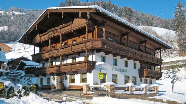 Un chalet traditionnel en bois, doté d’un balcon et entouré de montagnes enneigées.