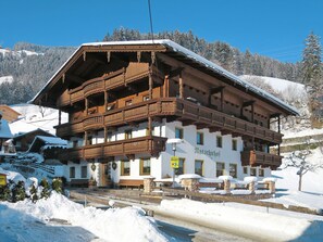 Un chalet traditionnel en bois, doté d’un balcon et entouré de montagnes enneigées.