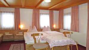 Une chambre d’hôtel confortable avec un lit en bois, deux tables de chevet, une petite table recouverte d’une nappe et une chaise.