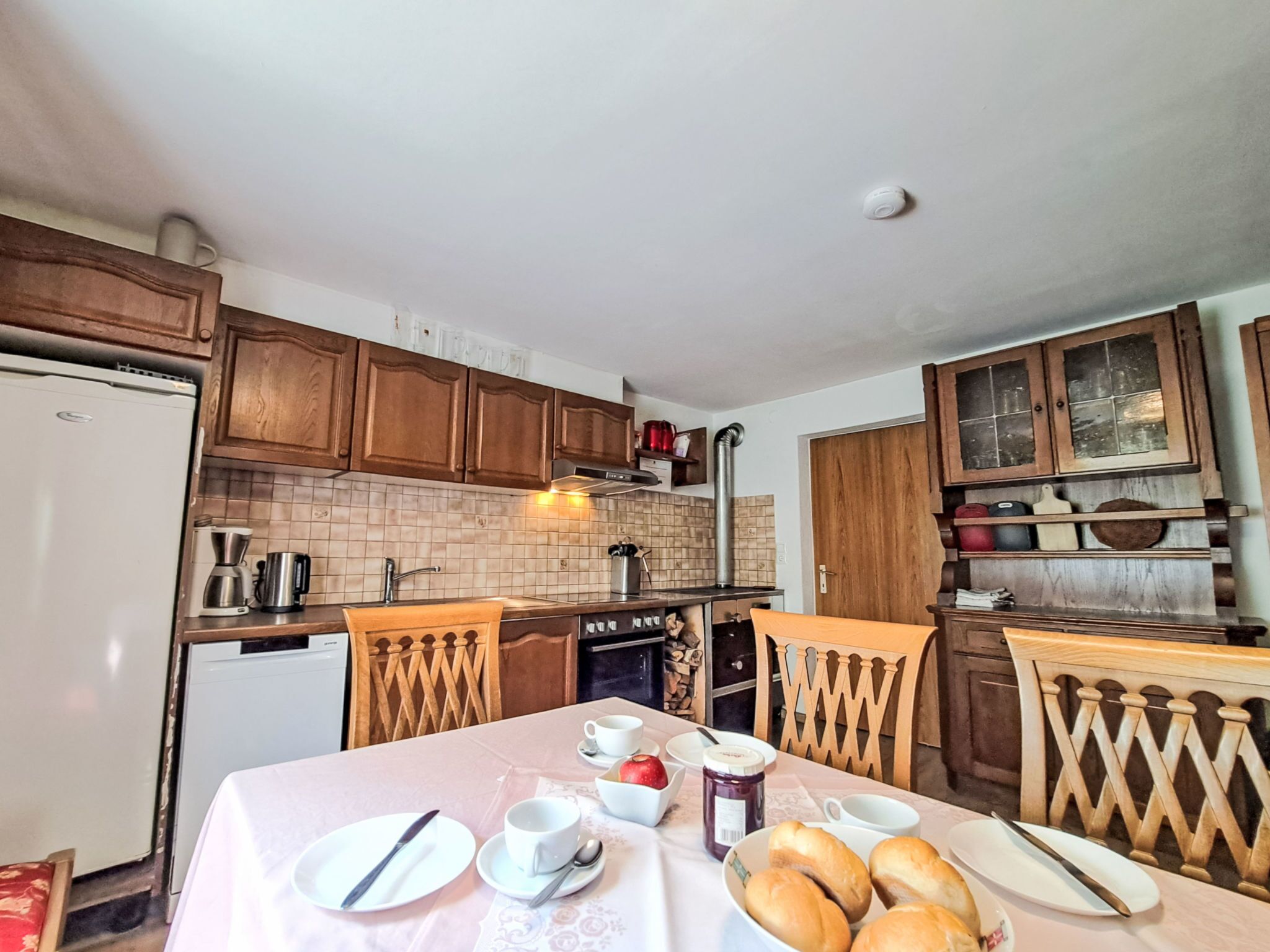 Une cuisine avec des meubles en bois, une cuisinière et une table à manger dressée avec des assiettes, des tasses et du pain.